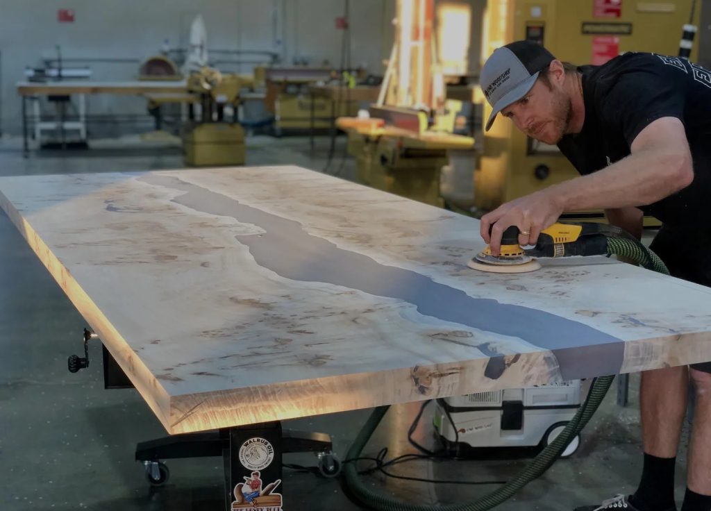 woodworker sanding solid wood epoxy table